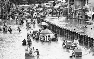  ?? — Reuters photo ?? Residents wade and ride on pedicabs along a partially flooded road, in Las Pinas Metro Manila as a storm sweeps across the main Luzon island, Philippine­s.