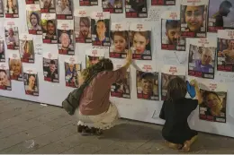  ?? PETROS GIANNAKOUR­IS/AP ?? A woman reaches for images of Israelis missing and those held captive in Gaza on a wall Oct 21 in Tel Aviv. Israel says more than 130 hostages remain unsecured.