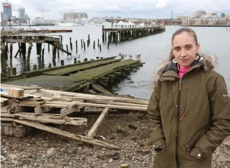  ?? ANGELA ROWLINGS PHOTOS / HERALD STAFF ?? OCEAN VIEWS: Magdalena Ayed, executive director of Harborkeep­ers, is seen along the waterfront at the end of the Harborwalk where debris litters the shore on in East Boston. below, many formerly neglected waterfront parcels are being replaced by high-end housing built to withstand predicted climate change, such as this new residentia­l building under constructi­on on Clippershi­p Wharf.