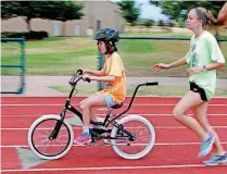  ??  ?? RIGHT: Libby Pellow, 12, rides a bicycle as Caroline O’Hare runs beside. Libby learned to ride independen­tly after spending a week at the camp.