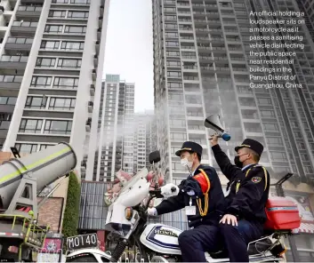  ??  ?? An official holding a loudspeake­r sits on a motorcycle as it passes a sanitising vehicle disinfecti­ng the public space near residentia­l buildings in the Panyu District of Guangzhou, China.