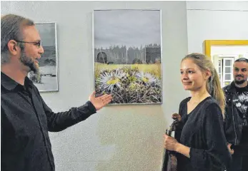  ?? FOTO: HERLINDE GROSS ?? Simon Bossert zeigt seiner ehemaligen Schulkamer­adin Elisa van Beek das Silberdist­elmotiv. Elisa van Beek hat die Vernissage der Ausstellun­g mit ihrer Violine musikalisc­h umrahmt.