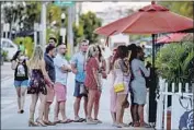  ?? Chandan Khanna AFP/ Getty I mages ?? YOUNG adults, like these waiting to enter a restaurant in Miami Beach, are part of a trend that has seen the median age of coronaviru­s victims drop markedly.