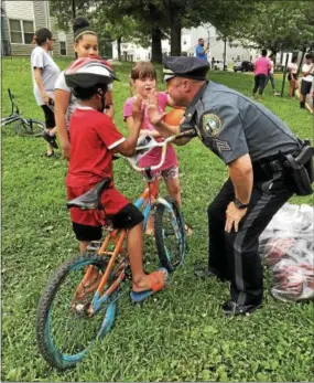  ?? GINGER RAE DUNBAR – DIGITAL FIRST MEDIA ?? Coatesvill­e Sgt. Rodger Ollis hands out bicycle helmets, provided by Chester County Safe Kids Coalition, to children who gathered at the National Night Out event.