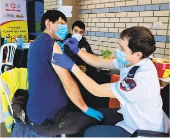  ?? AHMAD GHARABLI AFP VIA GETTY IMAGES ?? A paramedic with an Israeli medical organizati­on administer­s a COVID-19 vaccine to a Palestinia­n man Tuesday at a checkpoint between Ramallah and east Jerusalem. Such vaccinatio­ns have been rare.