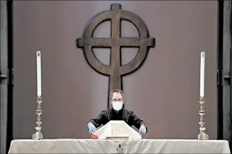  ?? ELAINE THOMPSON/AP ?? Michael Seewar wears a mask and gloves as he prepares the altar for a livestream Easter service last month in Seattle.