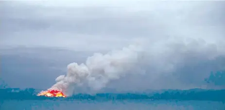  ??  ?? A fire in the distance seen from the Royal Australian Navy’s HMAS Adelaide ship off the coast in Eden in New South Wales, as part of bushfire relief operations.