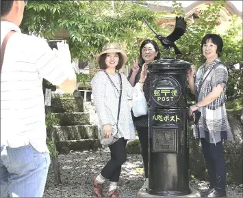  ??  ?? Women display amulets in front of a Yatagarasu statue at Kumano Hongu Taisha shrine in Tanabe, Wakayama Prefecture. — Japan News-Yomiuri photo