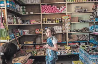  ??  ?? Nour Lazem, 10, who lost 16 members of her family in a suicide bombing, looks out at a shop in east Mosul.