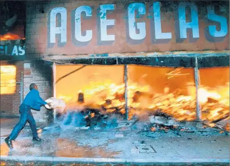  ?? Hyungwon Kang
Los Angeles Times ?? A SHOP OWNER hurls a bucket of water on a fire raging at the business next door to his on April 29, 1992, the first night of the Los Angeles riots. Several months after the unrest, city residents still felt wary and wounded, Times polling found at the...