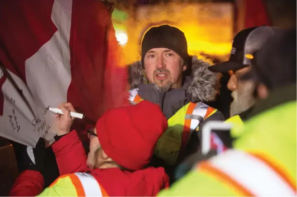  ?? PHOTOS: BRANDON HARDER ?? Rion White of Moose Jaw, centre, stands among the convoy supporters who signed a flag mounted on one of the trucks near Moose Jaw.