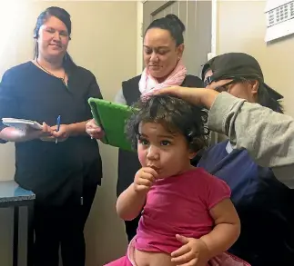  ?? CATHERINE GROENESTEI­N ?? Digital health deputy Janine Maruera takes a photo of a rash on Makaiah Nui’s neck, held by cousin Tesha Whakatutu, at the Maihealth clinic in Patea. Jeniveve Poari-Broughton watches on.