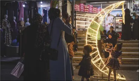  ?? ASSOCIATED PRESS ?? A Palestinia­n woman takes photos of her daughter next to a crescent moon-shaped decoration on Wednesday, in a market, at the beginning of the Muslim holy month of Ramadan in Jebaliya refugee camp, northern Gaza Strip.
