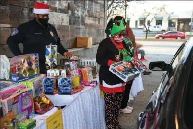  ?? The Sentinel-Record/Grace Brown ?? DRIVE-THRU TOYS: Sherry Wise with the Gateway Community Associatio­n, right, and Hot Springs police Cpl. Patrick Langley hand out gift bags to children during a drive-thru Christmas event in the parking lot behind 501 Prime, 215 E. Grand Ave., hosted by the Gateway Community Associatio­n on Monday.