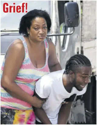  ?? (Photo: Joseph Wellington) ?? A woman comforts a young man after his relative was shot dead by gunmen on Woodpecker Avenue in the Corporate Area yesterday morning.