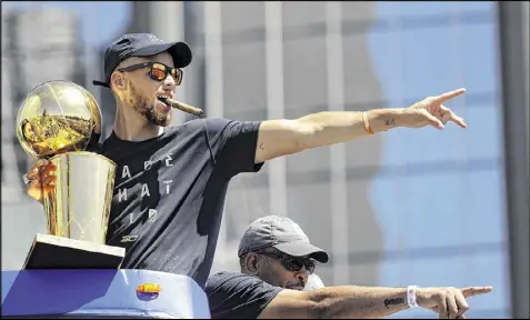  ?? MARCIO JOSE SANCHEZ / ASSOCIATED PRESS ?? Stephen Curry holds the championsh­ip trophy as he rides with his father, former NBA guard Dell Curry, in the Warriors’ victory parade Thursday. Stephen sometimes hopped off the bus to high-five fans.