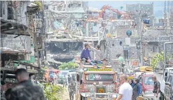  ??  ?? WHERE DO YOU START: Residents on top of their jeepney take photos of destroyed buildings during a visit to their homes at the main battle area in Marawi City.