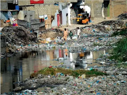  ?? — AFP ?? Youths search for their ball as they walk amongst dumped garbage at a residentia­l area of Karachi. Pakistan’s parliament passed a climate change bill on Friday as the country faces major climate-related problems.