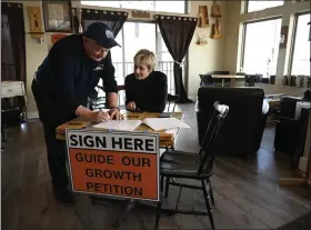  ?? RJ SANGOSTI — THE DENVER POST ?? Timnath resident Clifford Nancarrow, left, signs a petition Tuesday collecting signatures for a ballot measure that would ban fences taller than 65feet. Jacque Wilson, right, was part of a group of volunteers collecting the signatures for the ballot measure at Colorado Feed & Grain Coffeehous­e.