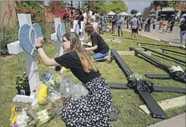  ?? Tony Gutierrez Associated Press ?? JENNIFER SEELEY signs a cross at a makeshift memorial created near a Dallas-area outlet mall where a gunman killed eight people on Saturday.