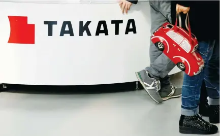  ??  ?? VISITORS WALK past a logo of Takata Corp. on its display at a showroom for vehicles in Tokyo in February.