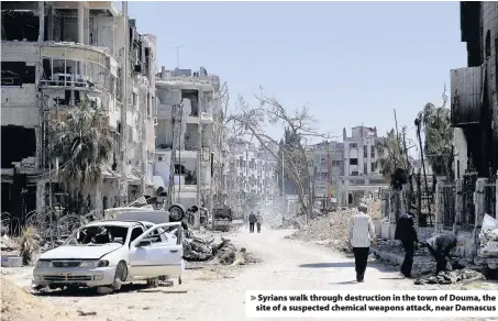  ??  ?? > Syrians walk through destructio­n in the town of Douma, the site of a suspected chemical weapons attack, near Damascus