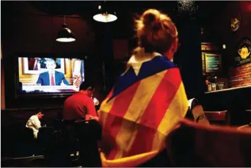  ?? PIERRE-PHILIPPE MARCOU/AFP ?? A woman wrapped in a Catalan pro-independen­ce flag listens to Spain’s King Felipe VI address the nation on a television set in a bar in Barcelona on Tuesday.