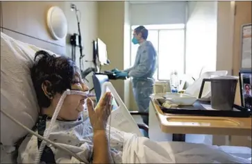  ?? Francine Orr Los Angeles Times ?? CAROLINA HENRIQUEZ, 66, blows a kiss while battling COVID-19 on Thursday at Providence Holy Cross Medical Center in Mission Hills. Chaplain Kevin Deegan, background, facilitate­s family visits over an iPad.