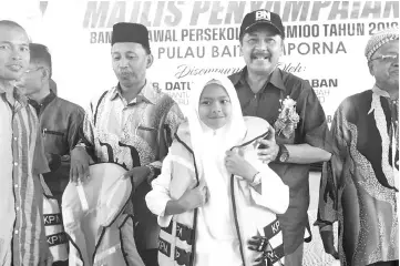  ??  ?? Ramlee presenting a safety jacket to a student at SK Pulau Bait during his visit.