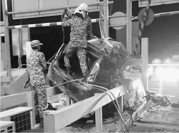  ??  ?? Fire and Rescue members try to extricate Chong’s body which was trapped in the driver’s seat. — Bernama photo