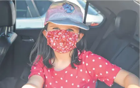  ??  ?? Six-year-old Eliza Boudreau shows off her floral mask, and pink unicorn cap, from the back seat of the family car after a shopping trip to a local megastore. DAVID JALA CAPE BRETON POST ■