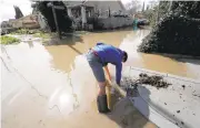  ?? LAURA A. ODA/STAFF ?? Gordon Smith tries to clear a storm drain as he and his neighbors begin to clean up on Brookwood Avenue.