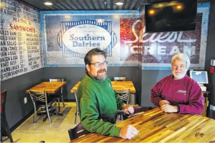  ?? STAFF PHOTO BY ERIN O. SMITH ?? Steve Flynn and Kerry Hoefer, co-owners of Stevarino’s, sit in their new restaurant on the North Shore in front of a reproducti­on of an old wall advertisem­ent. The location will be the third Stevarino’s with the others in South Pittsburg, Tenn., and in Scottsboro, Ala.