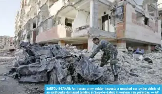  ??  ?? SARPOL-E-ZAHAB: An Iranian army soldier inspects a smashed car by the debris of an earthquake damaged building in Sarpol-e-Zahab in western Iran yesterday. — AP