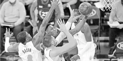  ?? KATHY WILLENS/ AP ?? Orlando Magic forward Dwayne Bacon, left, and center Nikola Vucevic, right, defend New York Knicks guard RJ Barrett, center, as Barrett goes up for a layup during the first half on Monday in New York.