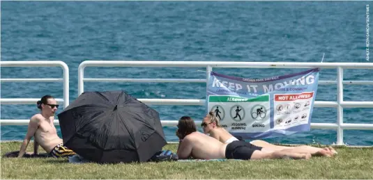 ??  ?? People sunbathe Monday near a “Keep It Moving” sign off the Lakefront Trail near West Diversey Parkway. With Chicago’s stretch of 90-degree days forecasted to continue through Friday, the city is opening cooling centers and other resources to help residents cope with the extreme heat.
