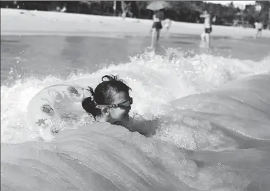  ?? SHA XIAOFENG / FOR CHINA DAILY ?? A child enjoys a cool moment in the ocean waves at a scenic zone in Sanya, Hainan province, on Sunday. Several cities in the province have issued
heat alerts recently.