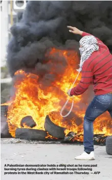  ?? AFP ?? A Palestinia­n demonstrat­or holds a sling shot as he runs past burning tyres during clashes with Israeli troops following protests in the West Bank city of Ramallah on Thursday. —