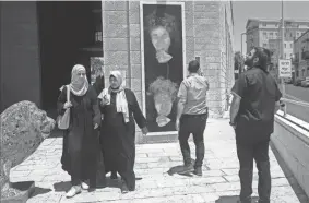  ?? JIM HOLLANDER/THE LONKA PROJECT VIA AP ?? People look at the defaced portrait of Holocaust survivor Peggy Parnass outside Jerusalem City Hall on July 1.