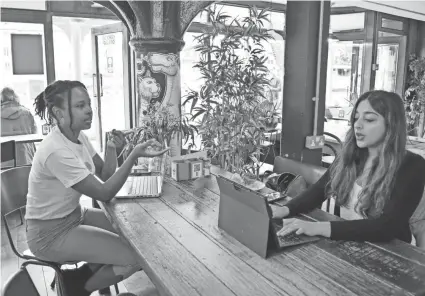  ?? UROOBA JAMAL/AP ?? Sonya Barlow, right, CEO of Like Minded Females Network, speaks to intern Rebekah Ingram at a coffee shop in London. Many young workers around the world have entered the workforce and begun their careers during the pandemic working entirely remotely.