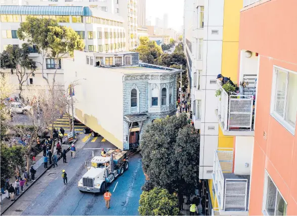  ?? BERGER/AP NOAH ?? Oversized load: A man watches Sunday as a truck pulls a Victorian home through the streets of San Francisco. The house, built in 1882, was moved about six blocks away to make room for a condominiu­m developmen­t. In preparatio­n for the move, which cost about $400,000, parking meters were removed, trees were trimmed and traffic signs were relocated.