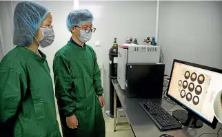  ?? AP ?? Zhou Xiaoqin, left, and Qin Jinzhou, who were part of the team working with scientist He Jiankui, inset, view a time lapse image of embryos on a computer screen at a laboratory in Shenzhen in southern China’s Guandong province.