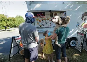  ?? (AP/Ted S. Warren) ?? Bobby Price and Catherine Vogt, along with Vogt’s daughter, Avery, 8, wait to order from a food truck earlier this month near the Seattle suburb of Lynnwood, Wash. More photos at arkansason­line. com/822food/.