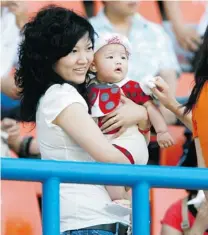  ??  ?? In this picture taken last June, Wang Ti holds her daughter during a football match in Dalian, China. Wang has been sentenced to life in jail for defrauding celebritie­s of nearly $ 10 million.