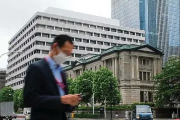  ??  ?? Boosting economy: A man walking past the Bank of Japan in Tokyo. Japan’s second record extra budget since April is widely seen as needed amid the nation’s worst economic crisis in decades, but it also adds to a mountain of public debt. — AFP