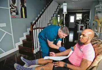  ?? BARBARA HADDOCK TAYLOR/BALTIMORE SUN ?? Dr. Chris Kircher, left, owner of Bmore Hydrated, places an IV in the arm of Ken Macon, a Realtor from Baltimore, as he receives IV vitamin and hydration therapy at his home.