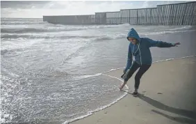  ?? Emilio Espejel, The Associated Press ?? Milagro de Jesus Henriquez Ayala dips her toes in the Pacific Ocean, just a few yards from the border wall that separates Mexico from the United States, in May at Playas de Tijuana, Mexico.