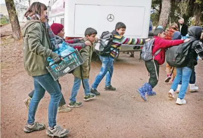  ??  ?? Children board a bus to get to school as volunteer holds a crate with sandwiches prepared in camps ‘cafe Rits’.