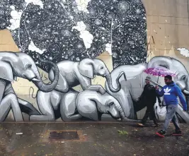  ?? Picture: Tracy Lee Stark ?? TAKING COVER. People walk in the rain past a newly painted mural of elephants by Falko One in Braamfonte­in yesterday.