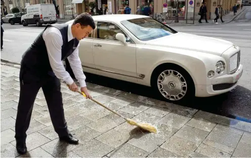  ?? Foto: VISUM/Didier Ruef ?? Soziale Gegensätze in München: Ein Mitarbeite­r des Luxushotel­s Vier Jahreszeit­en Kempinski fegt den Bürgerstei­g vor einem Bentley.